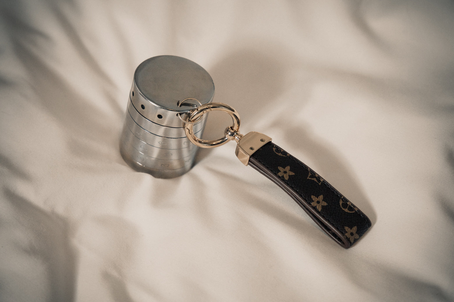 A sleek silver RockLock jewelry lockbox attached to a Louis Vuitton keychain rests on soft bedding. Designed for security and elegance, RockLock keeps valuable jewelry safe, stylish, and trackable at home or while traveling.