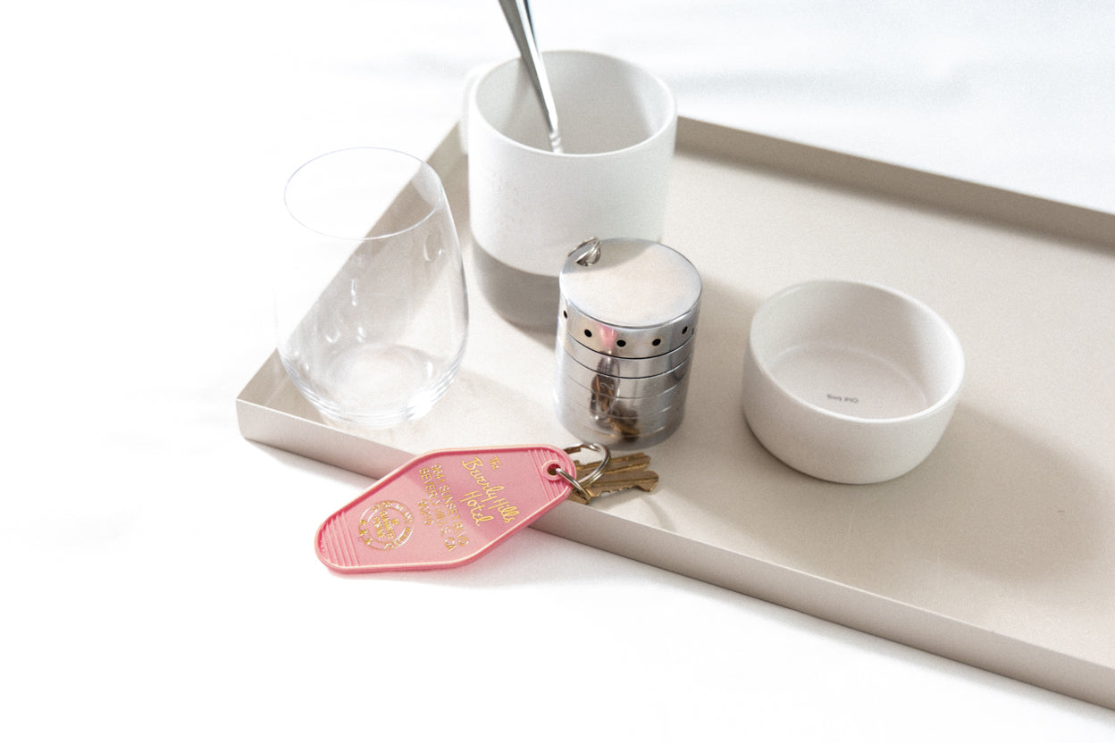 A sleek silver RockLock jewelry lockbox attached to a pink hotel key from The Beverly Hills Hotel, placed on a stylish breakfast tray. Designed for security and elegance, RockLock ensures valuable jewelry stays safe and trackable while traveling.