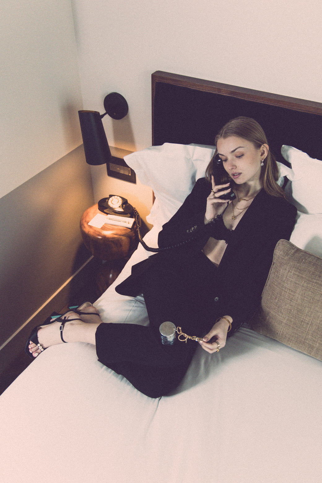 A stylish woman lounges in a hotel room, elegantly dressed in black while holding a RockLock jewelry lockbox with a gold keychain. Designed for security and sophistication, RockLock ensures valuable jewelry stays safe and trackable while traveling.