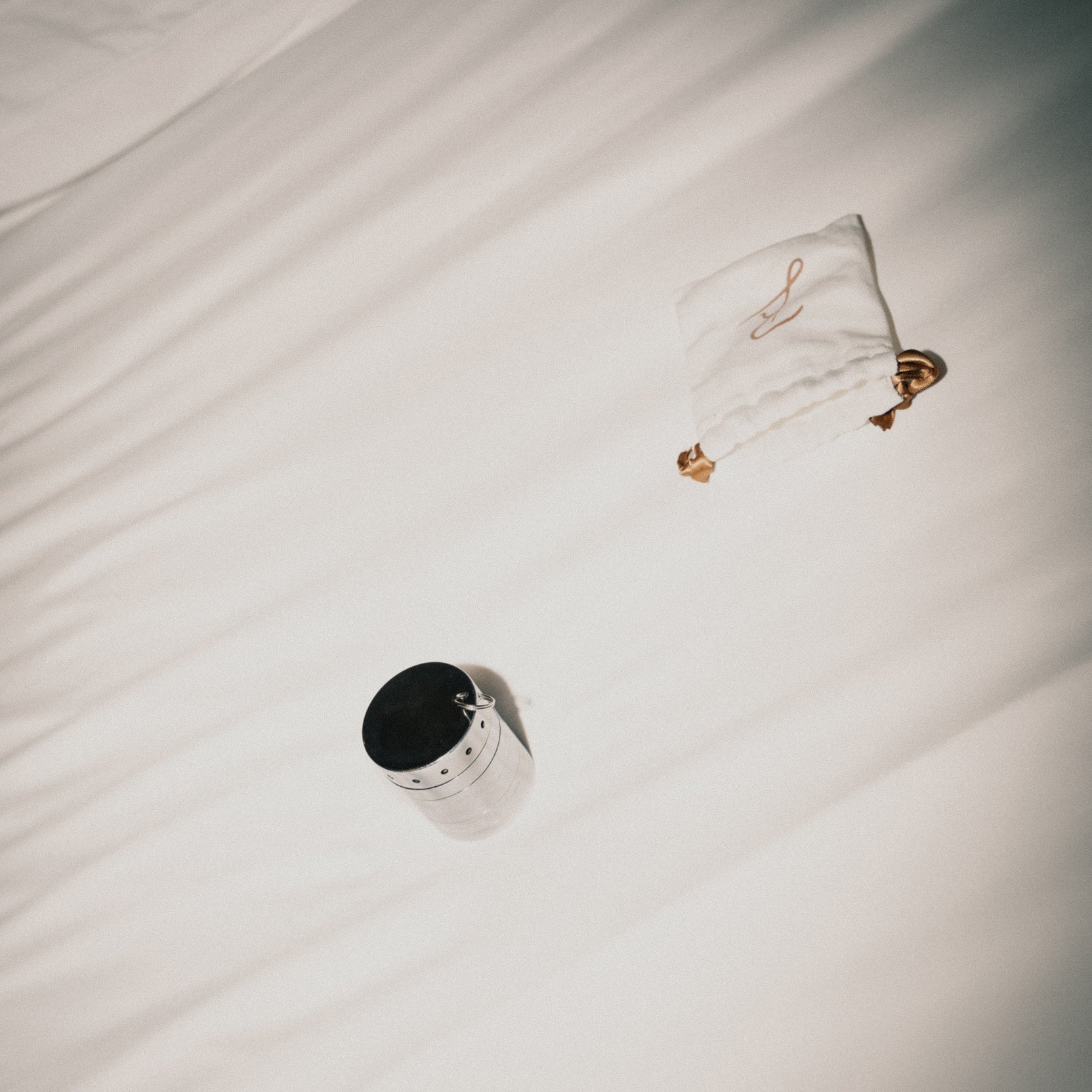 The Rock Lock jewelry security container resting on a soft, neutral-toned bed, next to its signature white drawstring pouch with gold accents—combining elegance with protection for valuable accessories.